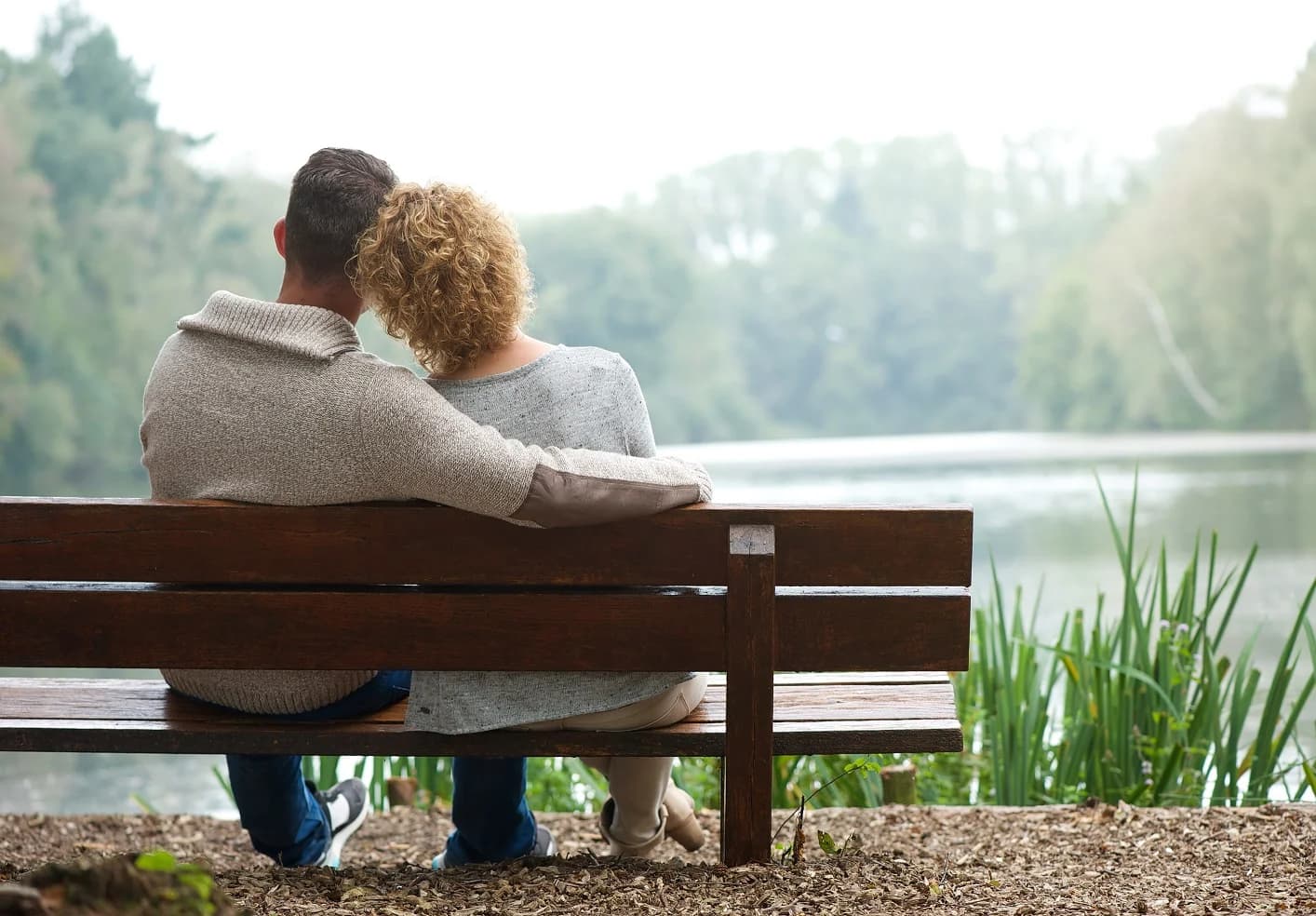 Man and woman sitting on bench facing blurred field with trees